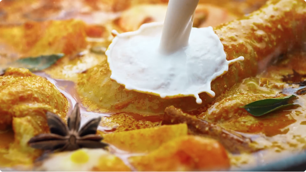 Coconut cream poured into a cooking pot of chicken curry in slow motion.