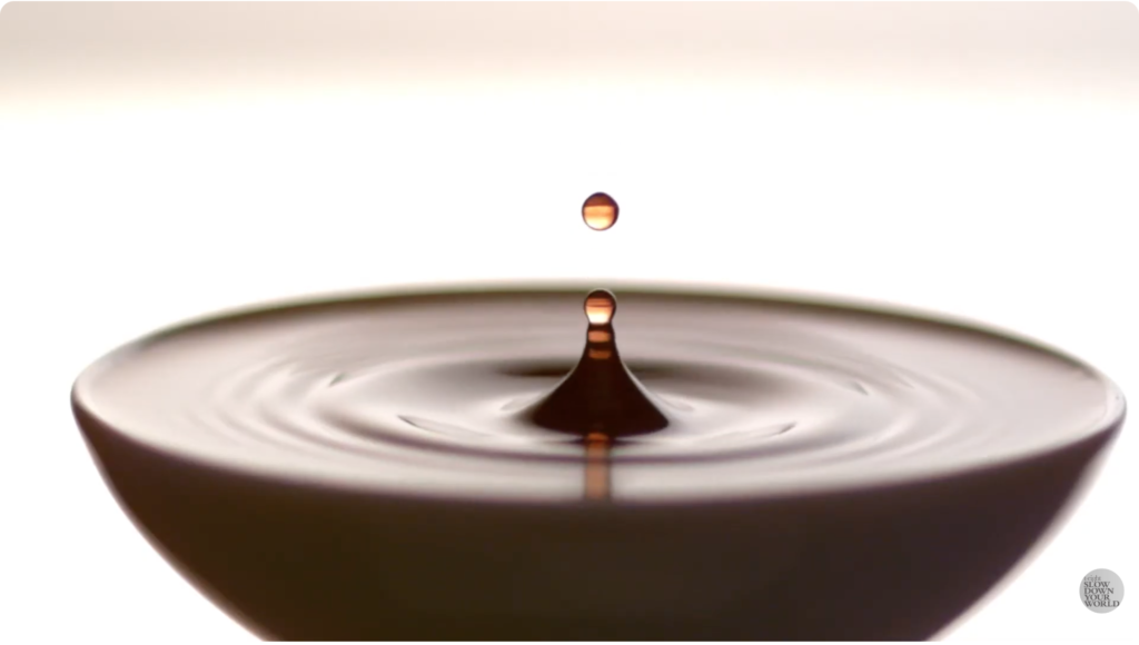 A droplet of wine falling into a wine glass in slow motion.